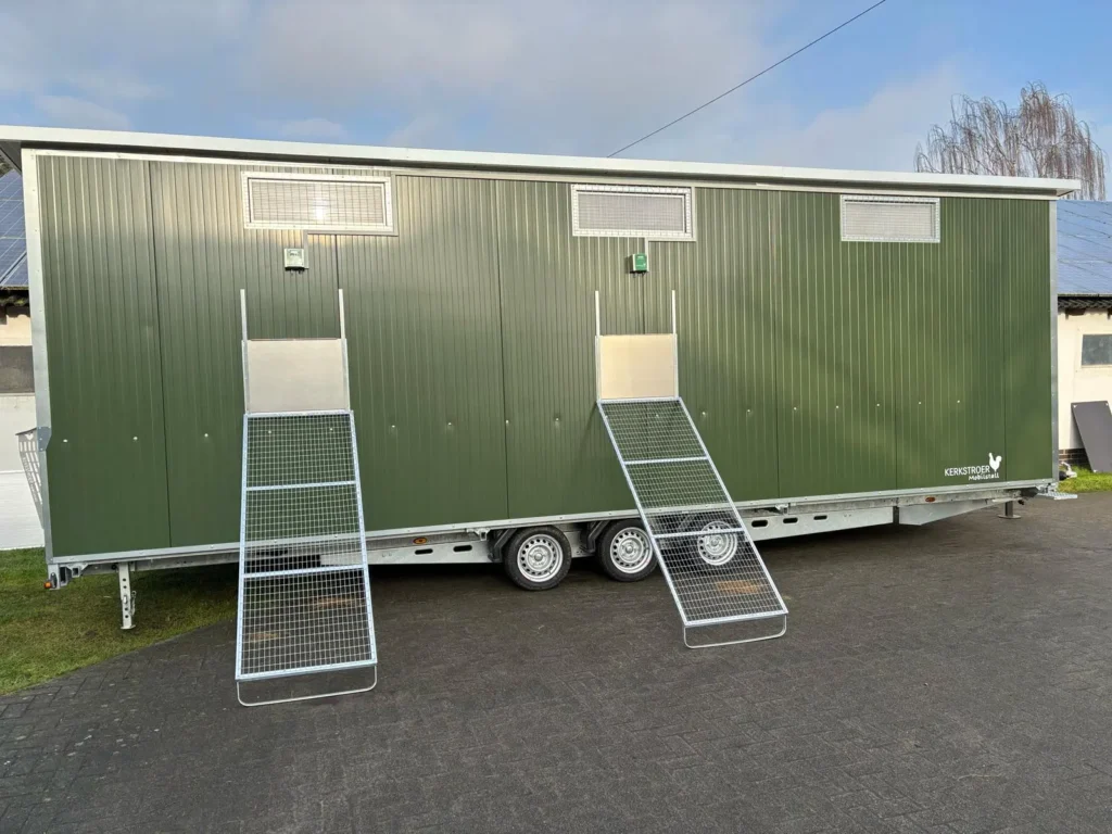 Eine seitliche Ansicht eines grünen Mobilstalls mit zwei Rampen und Fenstern, auf einem Anhänger stehend.