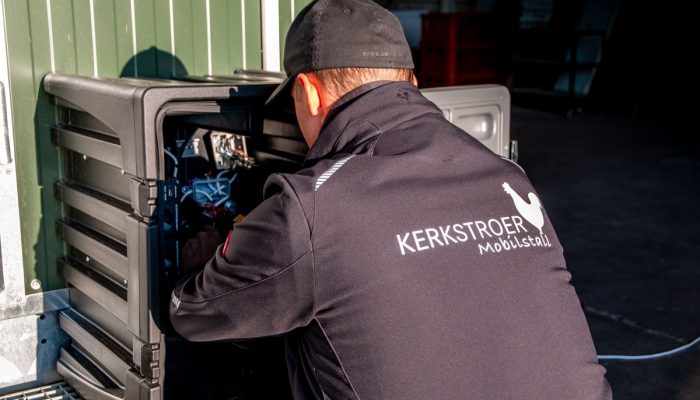 Ein Arbeiter von Kerkstroer Mobilstall wartet an einem mobilen Hühnerstall und ist mit der technischen Ausrüstung beschäftigt.