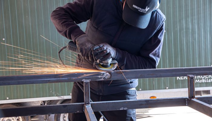 Ein Handwerker bearbeitet ein Metallgestell mit einer Winkelschleifmaschine, während Funken sprühen.