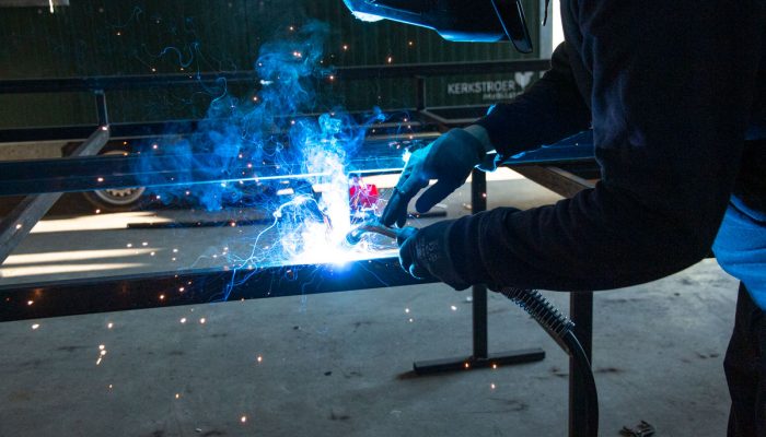 Ein Handwerker schweißt an einem Metallrahmen, während Funken und blauer Rauch aufsteigen.